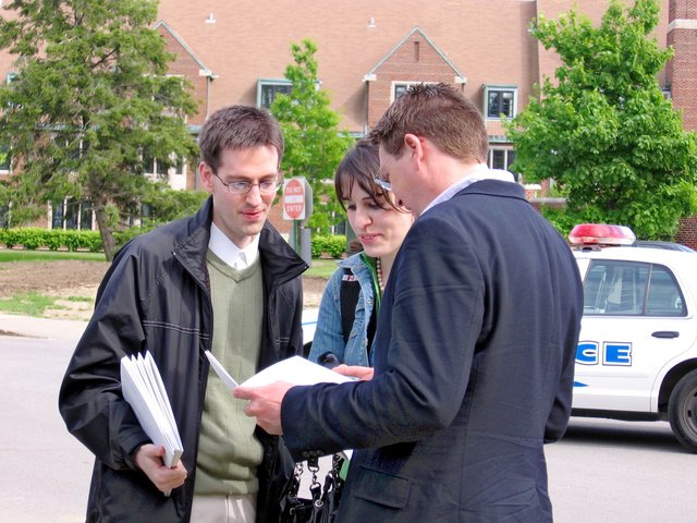 After commencement, near the Valparaiso U. Book Center--Isaac Sancken, Joni Sancken, and Steven Schumm--all visible to varying degrees--peruse one of many programs they collected from commencement (From Gregory Sancken)